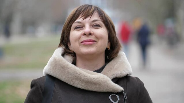 A beautiful European woman is standing in a black medical mask on the street. She looks at the camera and then takes off her mask and smiles. Close-up, shallow depth of field