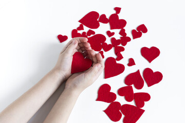 Children's hands, holding in open palms a bright red heart on a light background.