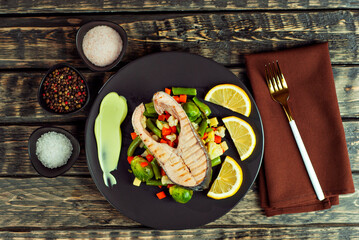 Grilled salmon steak. Red salmon with lemon and vegetables close up. wasps on a salad of boiled cabbage, carrots, green peas and broccoli. Food on shabby wooden table.