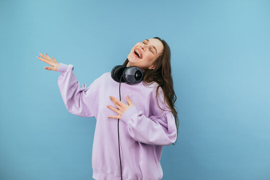 Cheerful girl in a purple sweatshirt and headphones is happy with a smile on his face and emotionally laughs on a blue background.