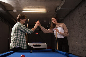Young couple high fiving each other, celebrating successful pool game