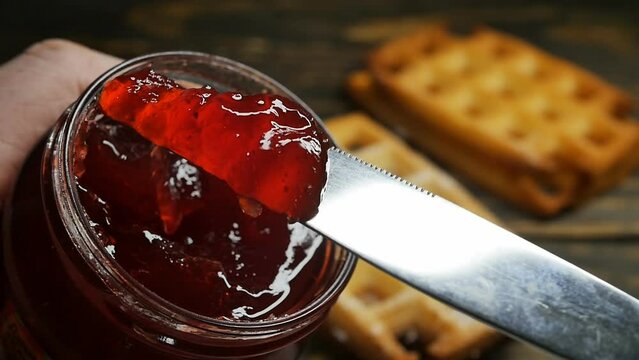 spreading strawberry jam from a jar on Belgian waffles with a table knife, slow motion