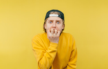 Close photo of a worried young man on a yellow background, biting his nails and looking scared at...