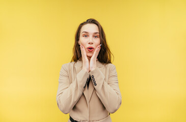 Joyful beautiful business lady in a jacket stands with a happy face on a yellow background and...