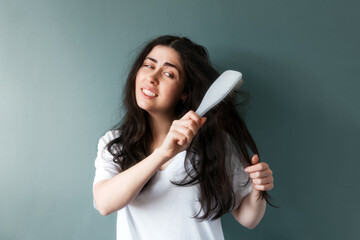 Portrait of a young sad woman trying to comb her long dark tangled hair with hairbrush. Blue...
