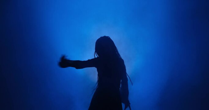 Silhouette of woman with long hair dancing in blue light and smoke