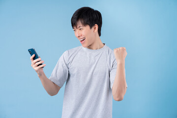 Young Asian man using smartphone on blue background - Powered by Adobe