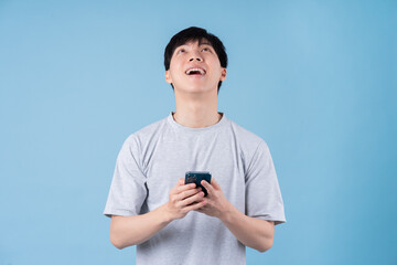 Young Asian man using smartphone on blue background