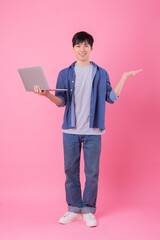 Young Asian man standing and using laptop on pink background