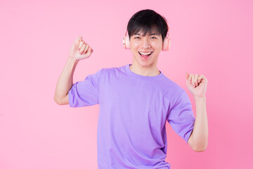 Young Asian man listening music on pink background