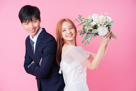 Young Asian bride and groom posing on pink background
