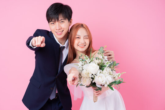 Young Asian bride and groom posing on pink background