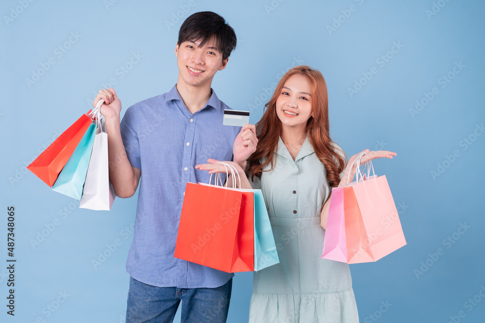 Canvas Prints Young Asian couple carrying shopping bag on blue background