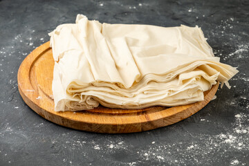 Thin filo dough for baking on a wooden board, dark table. Raw filo dough.