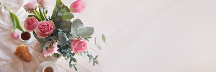 Pink background with bouquet of spring flowers on white breakfast table. Horizontal top view with short depth of field and space for text greetings.