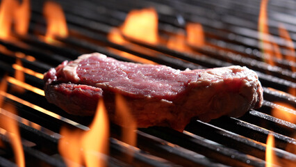 Grilling raw steak meat beef on flaming grill.