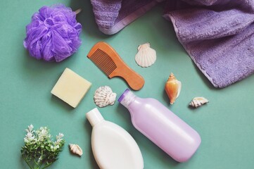 Purple towel, soap bar, shampoo bottle, shower gel, wooden comb and flower. Flat lay object photography organic natural cosmetics for hair and skin care