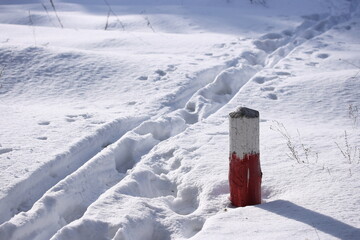 Ski track and footprints in the snow near a red and white wooden pole