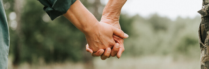 happy senior couple holding hands. hands of man and woman hold each other. romance and love and support in elderly family. faceless husband and wife travel together in nature. countryside life. banner - Powered by Adobe