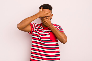 young afro man covering face with both hands saying no to the camera! refusing pictures or...