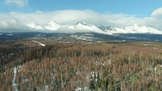 Aerial drone view of High Tatras mountains panorama, Slovakia. Mountain peaks covered with snow in winter. Forest and wild nature, blue sky with clouds. Vysoke Tatry in local speak.