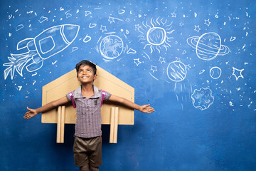 happy kid with cardboard rocket on back with space, universe and planets doodle drawing on wall -...