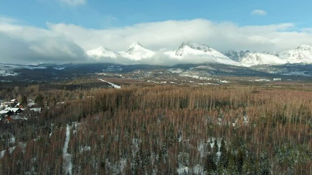 Aerial drone view of High Tatras mountains panorama, Slovakia. Mountain peaks covered with snow in winter. Forest and wild nature, blue sky with clouds. Vysoke Tatry in local speak.