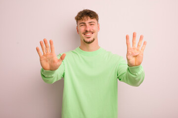 young cool man smiling and looking friendly, showing number nine or ninth with hand forward,...