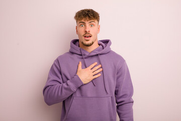 young cool man feeling shocked, astonished and surprised, with hand on chest and open mouth, saying...