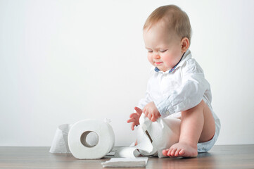Handsome blonde toddler in shirt and toilet paper rolls with potty. Potty training...