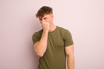 young cool man feeling disgusted, holding nose to avoid smelling a foul and unpleasant stench