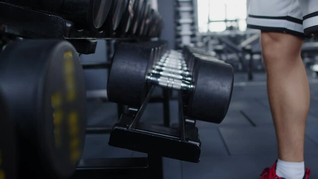 Closeup of male powerlifters hand taking dumbbell from drain in gym, side view. Male bodybuilder takes dumbbells from rack in gym