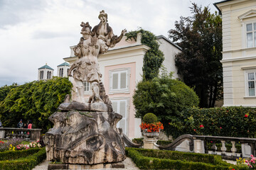 Salzburg, Austria, 28 August 2021: Famous Mirabell gardens near palace, geometrically arranged park, Baroque stone statue of the abduction of Helena at summer day, Sound of Music, Red roses