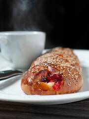 Sweet bread stuffed with strawberry jam and cheese, with sesame seeds, traditional Mexican bread from Oaxaca, a steaming cup of coffee ior hot chocolate in the background.