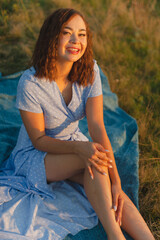 A girl of Asian appearance in a blue dress, resting in nature during sunset.