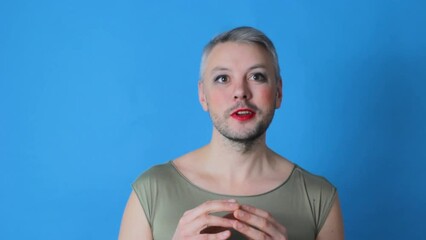 a gay man with makeup on his face talks looking at the camera on an isolated blue background. LGBT. Transgender