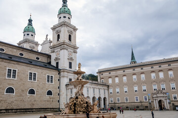 Salzburg, Austria, 28 August 2021: Fountain Residenzbrunnen with Triton statue at Domplatz square, Baroque cathedral with two white towers at summer day, Renaissance Alte Residenz or Old Residence