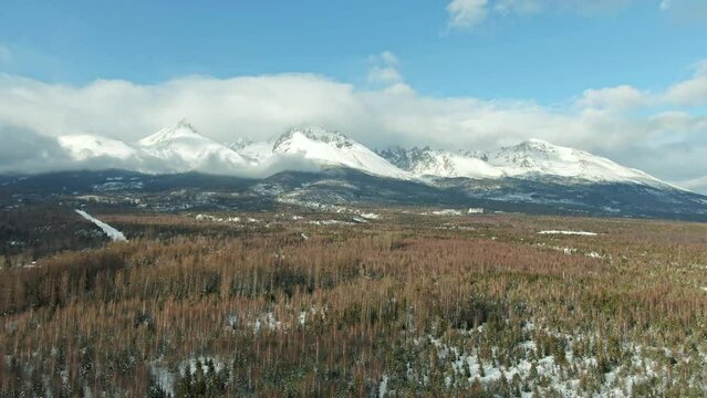 Aerial drone view of High Tatras mountains panorama, Slovakia. Mountain peaks covered with snow in winter. Forest and wild nature, blue sky with clouds. Vysoke Tatry in local speak.
