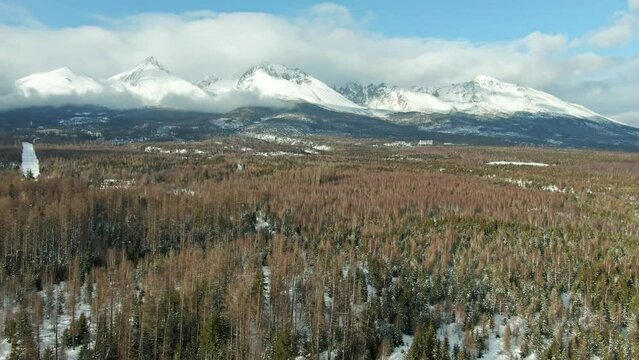 Aerial drone view of High Tatras mountains panorama, Slovakia. Mountain peaks covered with snow in winter. Forest and wild nature, blue sky with clouds. Vysoke Tatry in local speak.