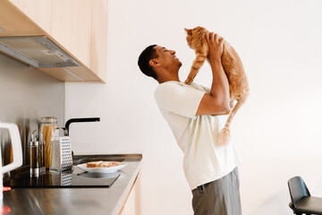 Black man playing with his cat while making breakfast