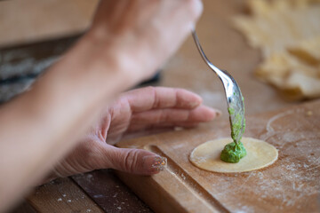 woman carries with spoon spinach filling for dumplings in round shape on wooden board in kitchen