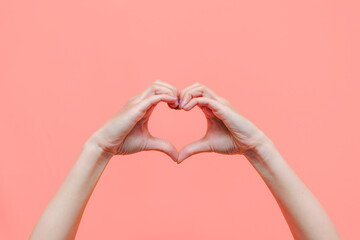 Female hands showing a heart shape isolated on a color light pink background. Sign of love,...