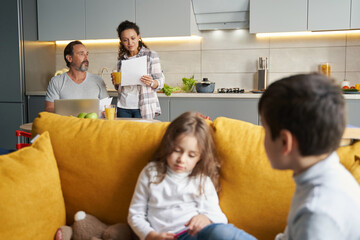 Female checking paper near husband with kids on sofa