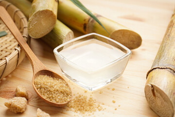 Sugarcane, fresh cane juice and brown sugar on a wooden background, close-up.