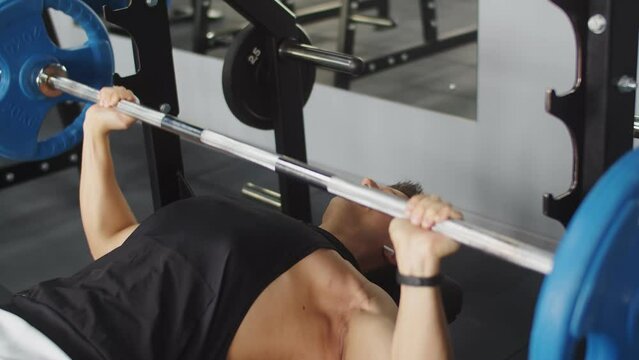 Male Bodybuilder Trains In Gym With Barbell In Prone Position On Bench, Front View. Athletic Man Lifts Barbell At Gym. Concept Training And Weightlifting