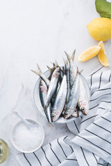 Fresh sardines, lemon and salt on white marble background. Still life with fresh seafood, sea fish, full of omega 3 and micro elements. Healthy food