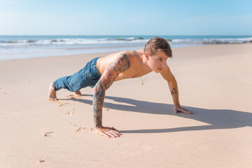 Fototapeta na wymiar Handsome young caucasian bare-chested man doing push ups on the beach