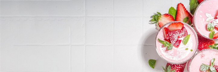 Homemade sweet strawberry panna cotta dessert, pink Italian panna cotta in three glasses, with fresh sliced strawberry and mint on white tiled background copy space