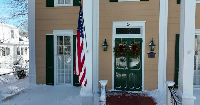 Large American home in winter snow. USA flag at front porch. Christmas decoration. Aerial truck shot in small town America.