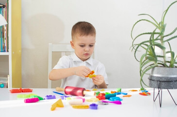 boy plays and creates from plasticine or clay. Cute child sculpts from plasticine on the table. The hands of a small child playing with a colorful modeling dough. Selective focus